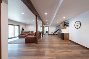 A spacious living area with a large sofa, a dining area with a kitchen, and a slide leading to a balcony. - Secluded Lakefront Retreat on 14 Acres with Private Boathouse & Firepit (St. Germain)