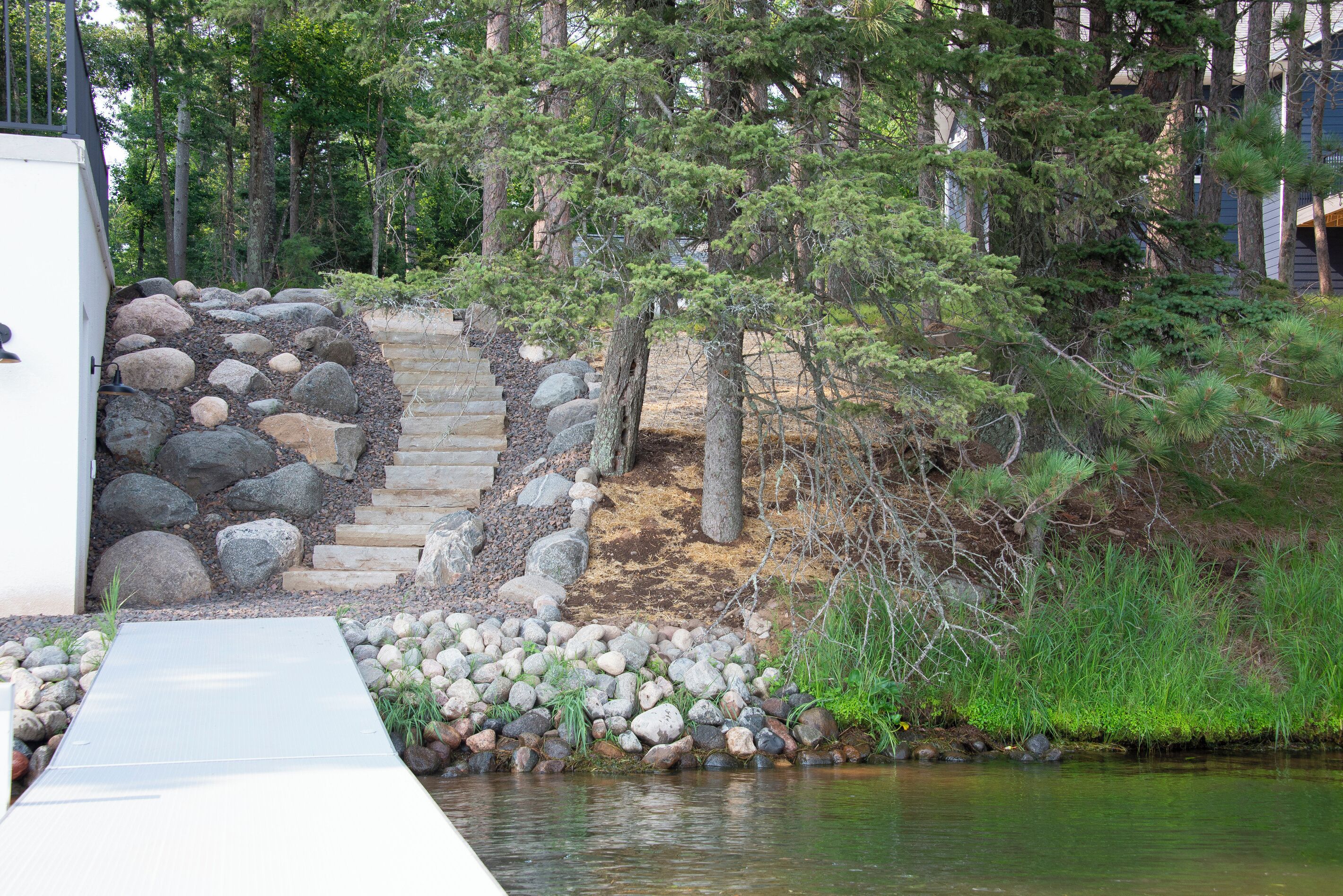 A wooden deck leading to a stone staircase surrounded by rocks and pine trees.