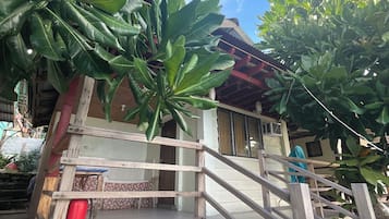 Una escalera de madera con barandilla, rodeada de abundante follaje verde, que conduce a un edificio con tejado de baldosas.