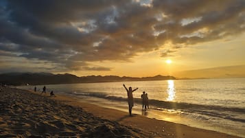 Una playa con gente, un atardecer y montañas al fondo.