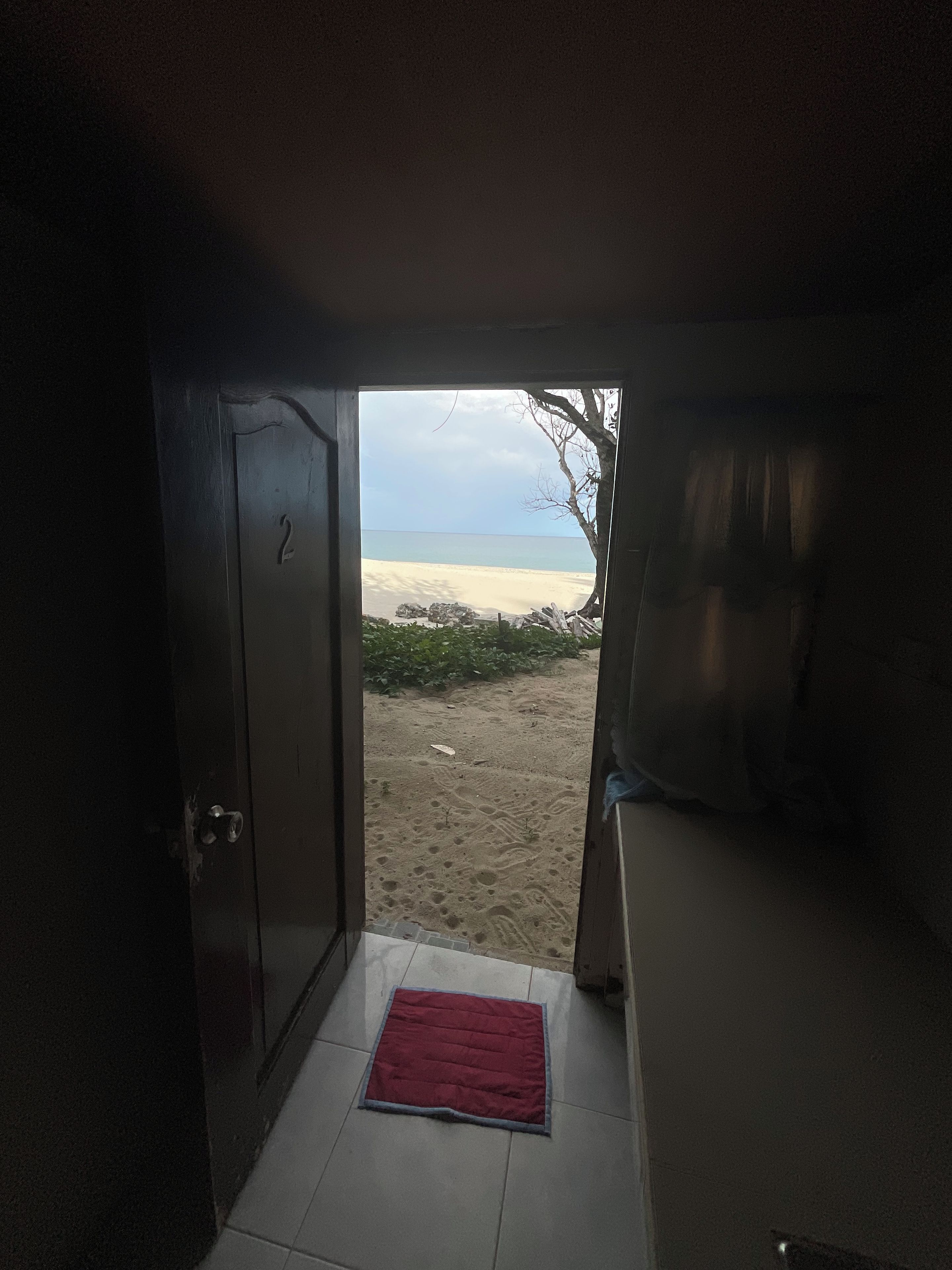 An interior space with a door leading to a sandy beach.