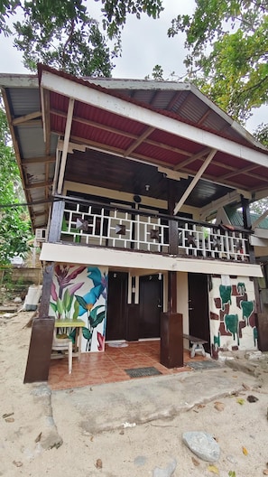 A two-story building with a balcony, a tiled entrance, and a mural on the lower wall.