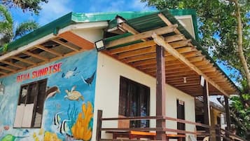 Un edificio con un mural de vida marina en la pared, un porche cubierto y suelo de arena.