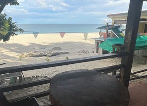 A beach view from a balcony with a view of the sea, a sandy beach, and a building with a green awning. - Diva Sunrise Beach Resort (Dipaculao)