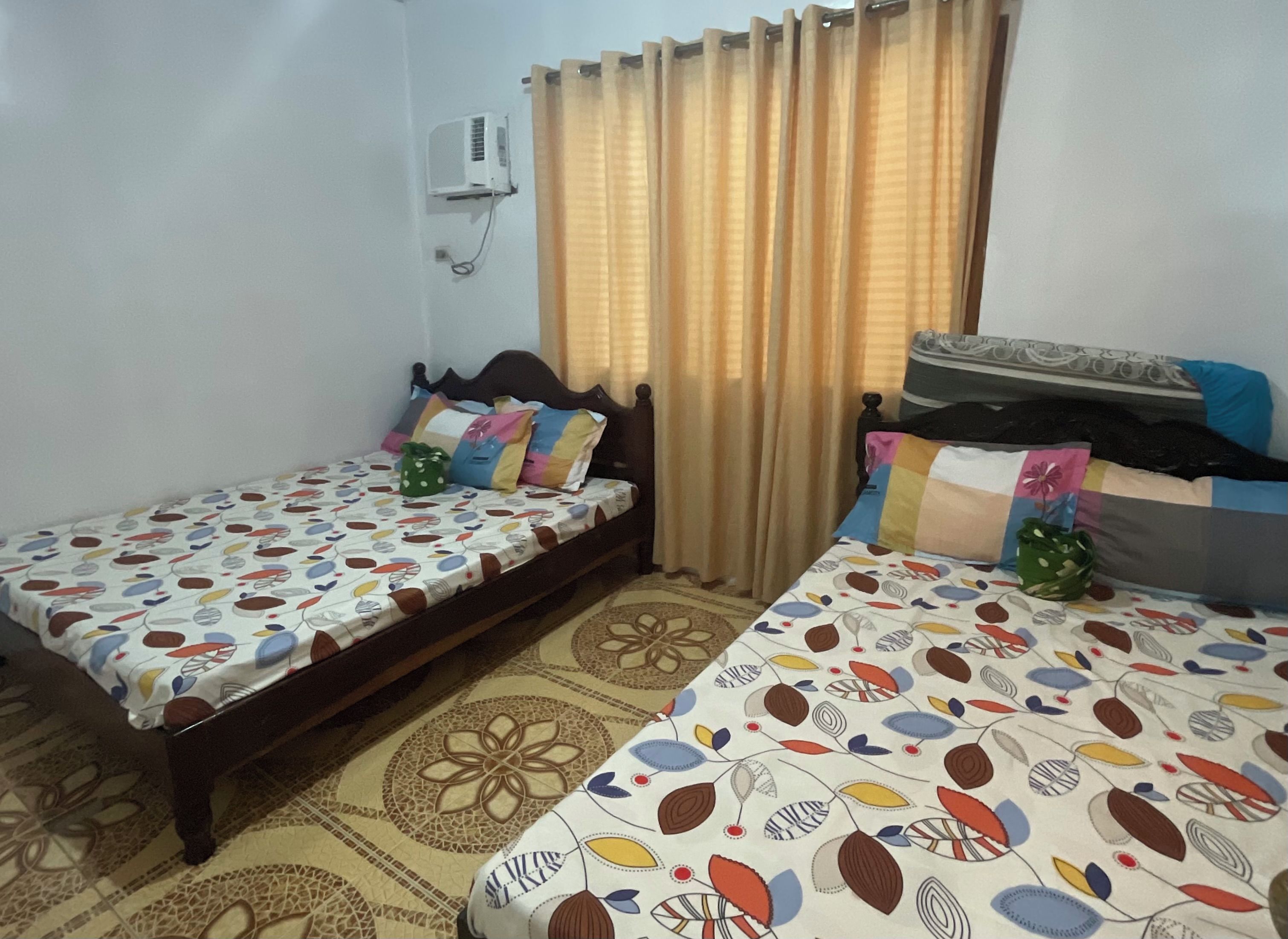 Una habitación con dos camas, cada una con ropa de cama estampada, un aire acondicionado de pared y una cortina.