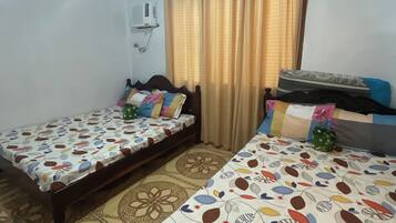 Una habitación con dos camas, cada una con ropa de cama estampada, un aire acondicionado de pared y una cortina.