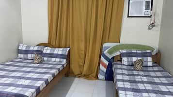 A room with two single beds, a window with curtains, a wall-mounted air conditioner, and a tiled floor.