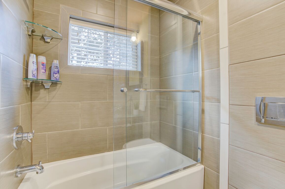 A modern bathroom with a glass-enclosed shower, a bathtub, and a shelf with toiletries.