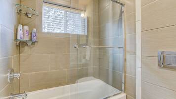 A modern bathroom with a glass-enclosed shower, a bathtub, and a shelf with toiletries.