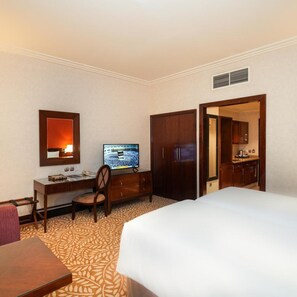 A hotel room with a bed, a desk with a chair, a television, a wardrobe, and a kitchenette. - Saja by Warwick, Makkah (Makkah)