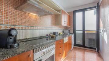 Una cocina con salpicadero de azulejos, encimera de granito, electrodomésticos de acero inoxidable, armarios de madera y una puerta corrediza de vidrio que da a un balcón.