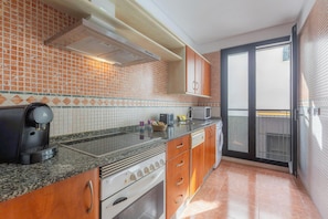 A kitchen with a tiled backsplash, granite countertop, stainless steel appliances, wooden cabinets, and a sliding glass door leading to a balcony. - Apt Blueseas Bahia Marina (El Puerto de Santa Maria)