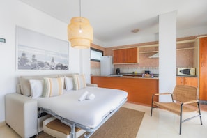 Ein kleines Hotelzimmer mit einem Bett, einem Sessel, einer Küchenzeile und einem Essbereich.