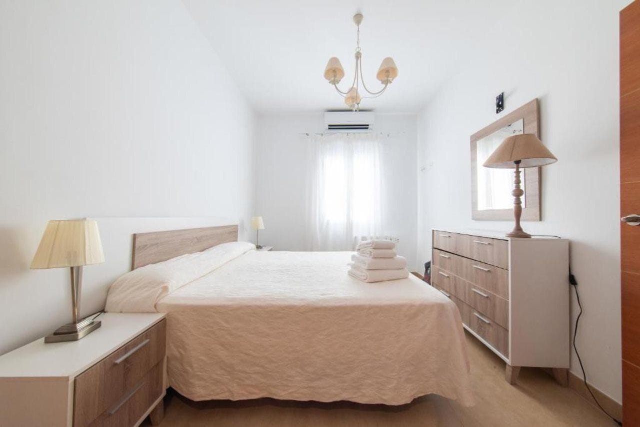 Una habitación de hotel con cama, mesitas de noche, lámpara, cómoda y espejo.