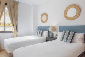 Ein Hotelzimmer mit zwei Betten, einem Fenster mit Vorhängen, einem Nachttisch mit Lampe und zwei runden Wandspiegeln.