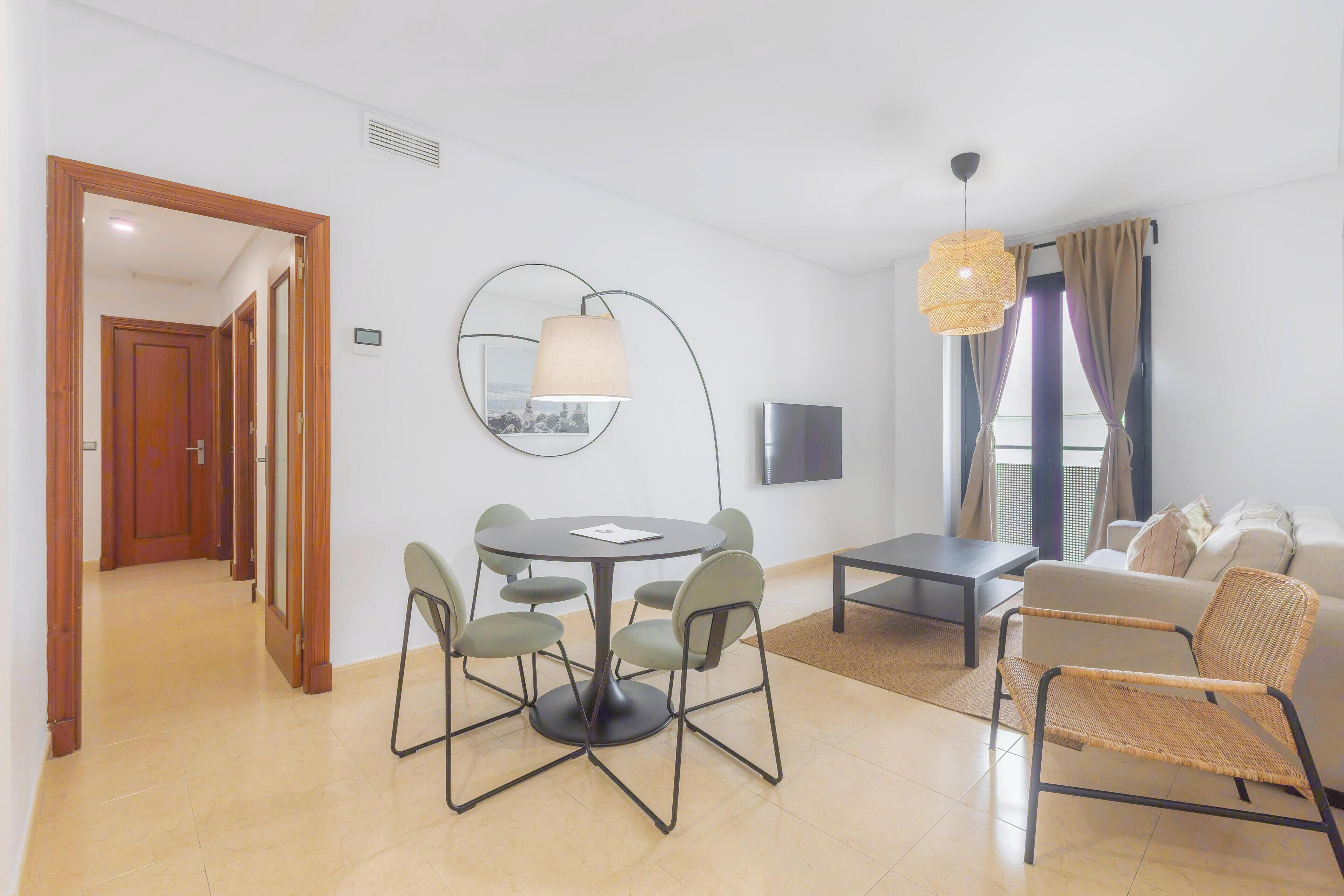 Una sala de estar moderna con una mesa de comedor redonda, sillas, un sofá y un televisor.
