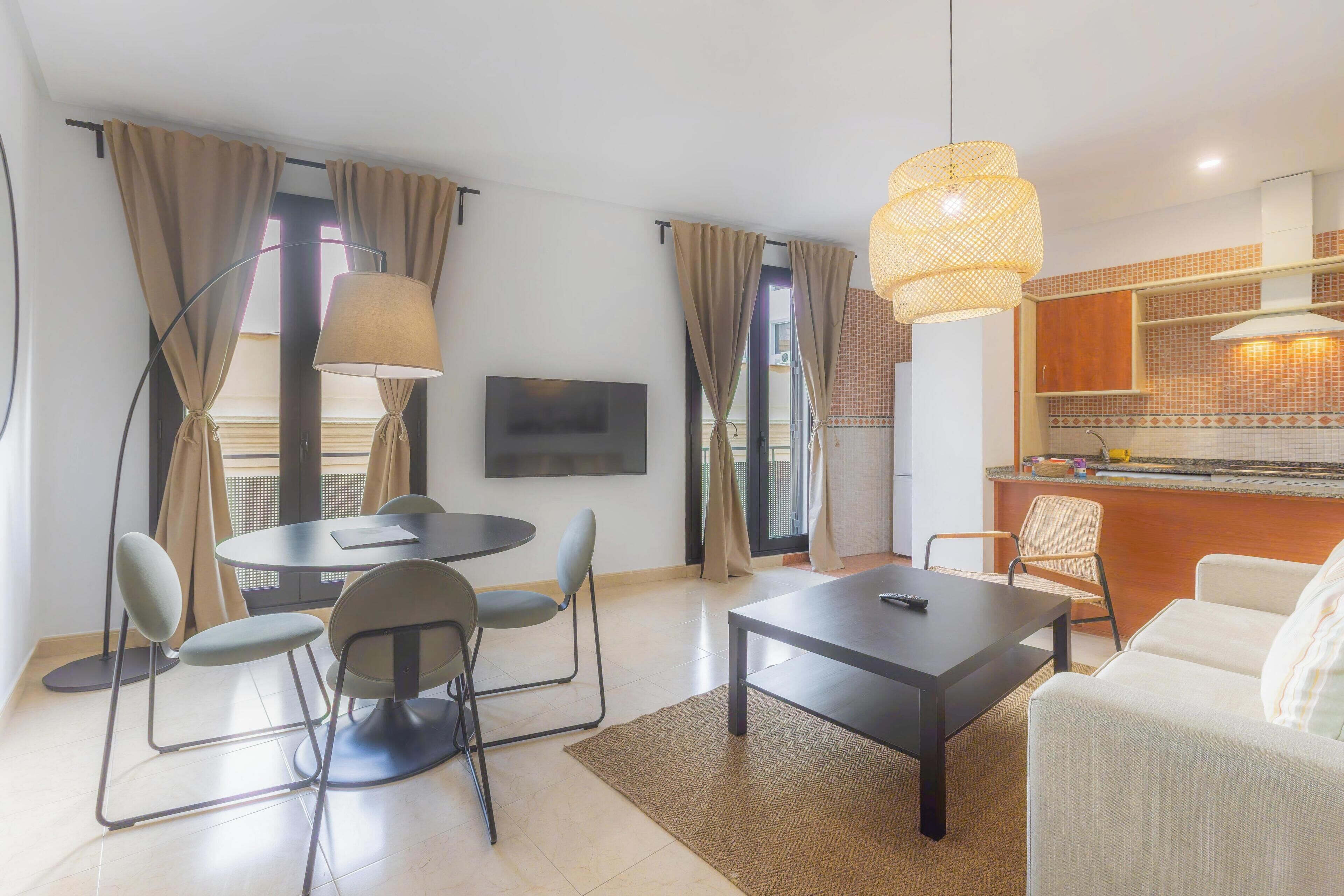 Una sala de estar moderna con una mesa de comedor redonda, un sofá y una zona de cocina con mostrador y armarios.