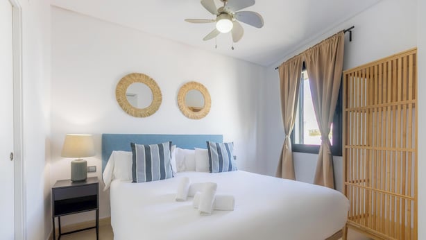 A neatly made bed with white linens and two round wall mirrors, a bedside lamp, and a wooden wardrobe.