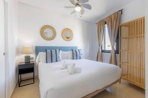 Una cama bien hecha con sábanas blancas, dos espejos redondos en la pared, una lámpara de noche y un armario de madera.