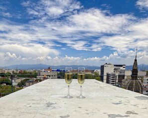 Two glasses of white wine on a rooftop terrace with a cityscape and mountains in the background. - Chic Roma Norte Penthouse Loft  AC & Parking (Ciudad de México)