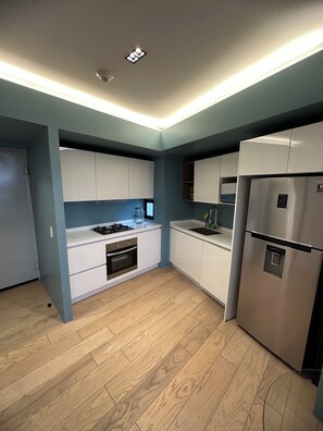 Una cocina moderna con armarios blancos, un refrigerador de acero inoxidable y un horno empotrado.