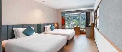 Une chambre d’hôtel avec deux lits, une petite table, une chaise et une grande fenêtre donnant sur un paysage verdoyant.