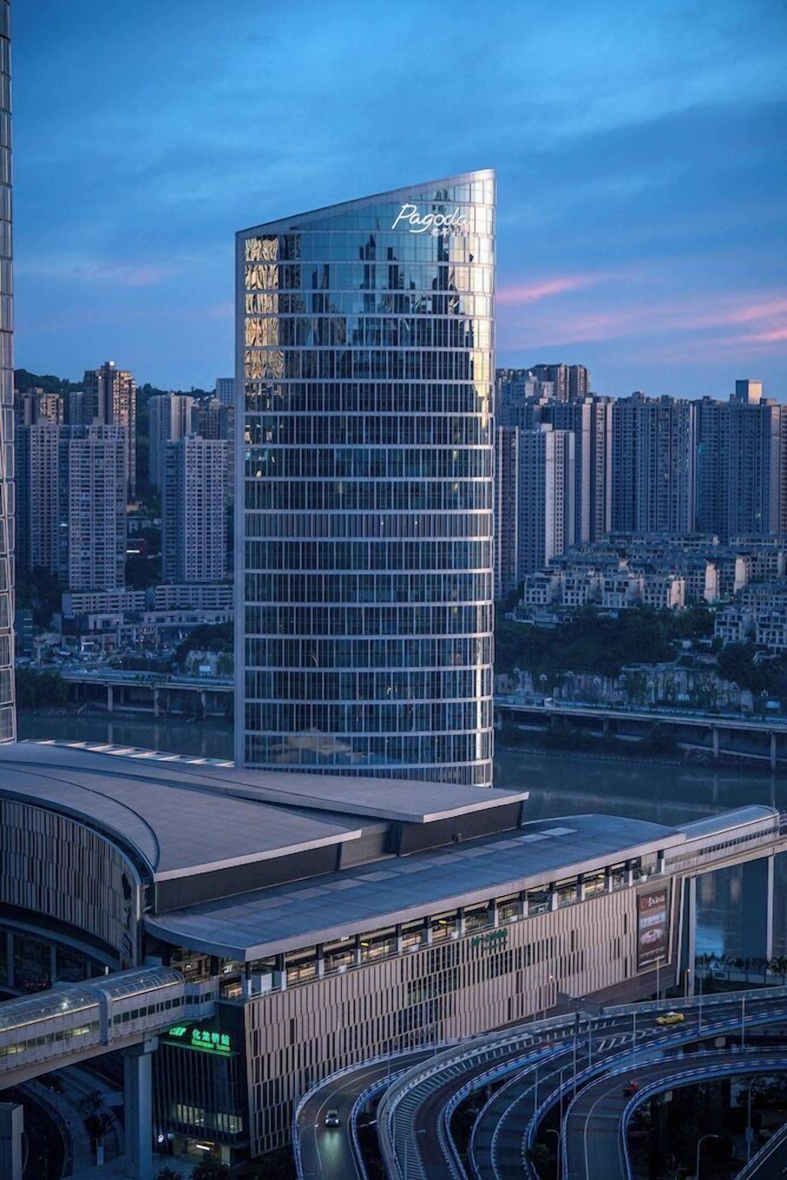 A modern high-rise building with a reflective glass facade, surrounded by a complex of lower buildings and a multi-level transportation hub with curved walkways.