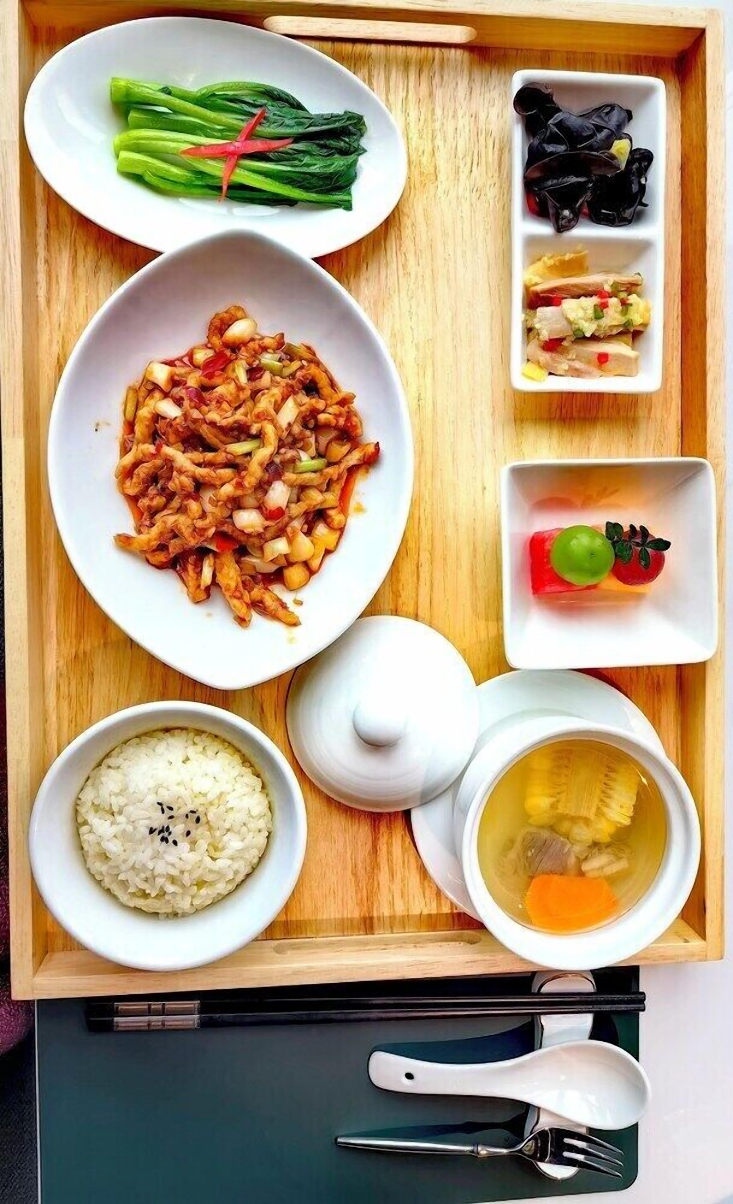 A wooden tray with various dishes including stir-fried vegetables, a bowl of rice, and a soup.