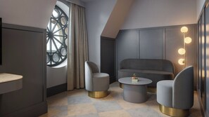 A modern room with a round window, two armchairs, a sofa, a small table, and a mirror with lights.