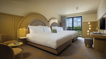 Una habitación de hotel con una cama grande, dos mesitas de noche, una zona de estar con una silla, un tocador con espejo y un televisor.