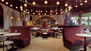L’intérieur d’un restaurant avec des tables rondes, des banquettes rouges recouvertes de tissu, des suspensions décoratives et des éléments de décoration florale.