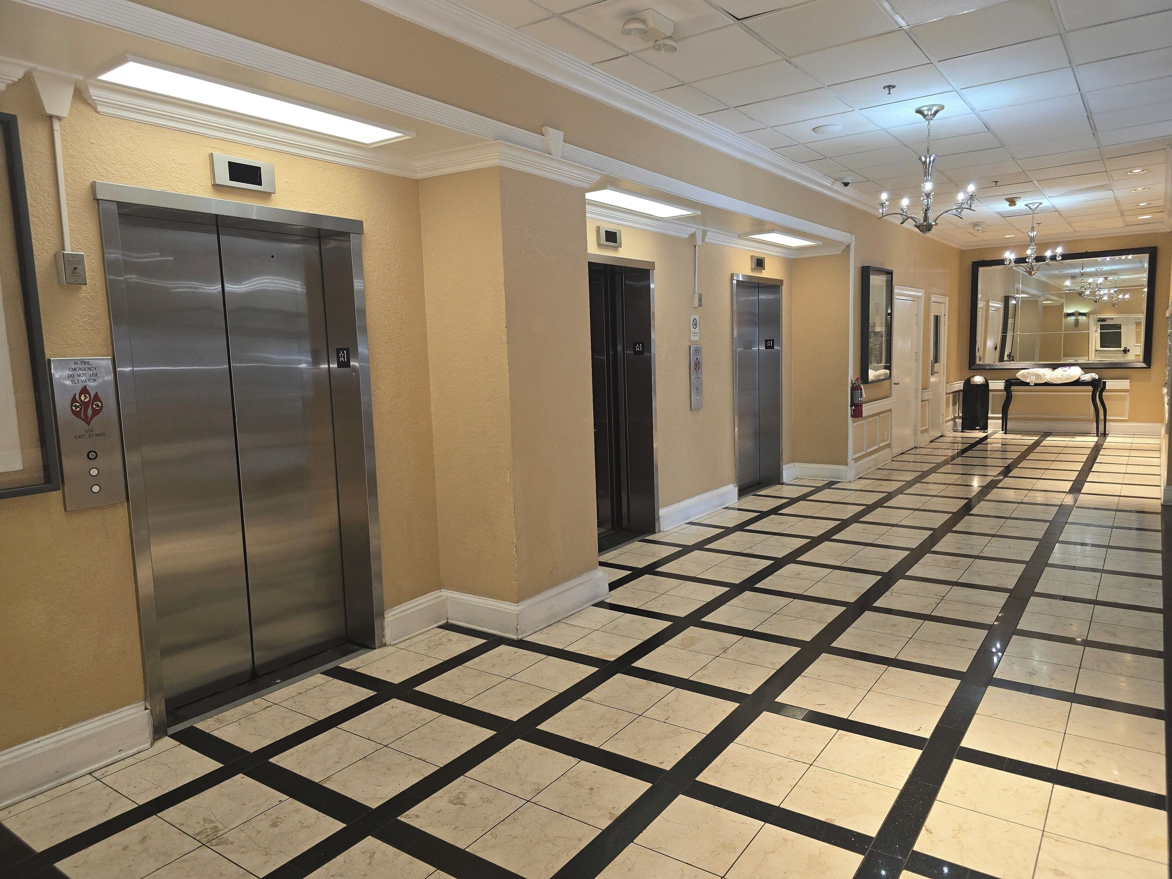 Pasillo de hotel con ascensores, un banco y piso de baldosas.