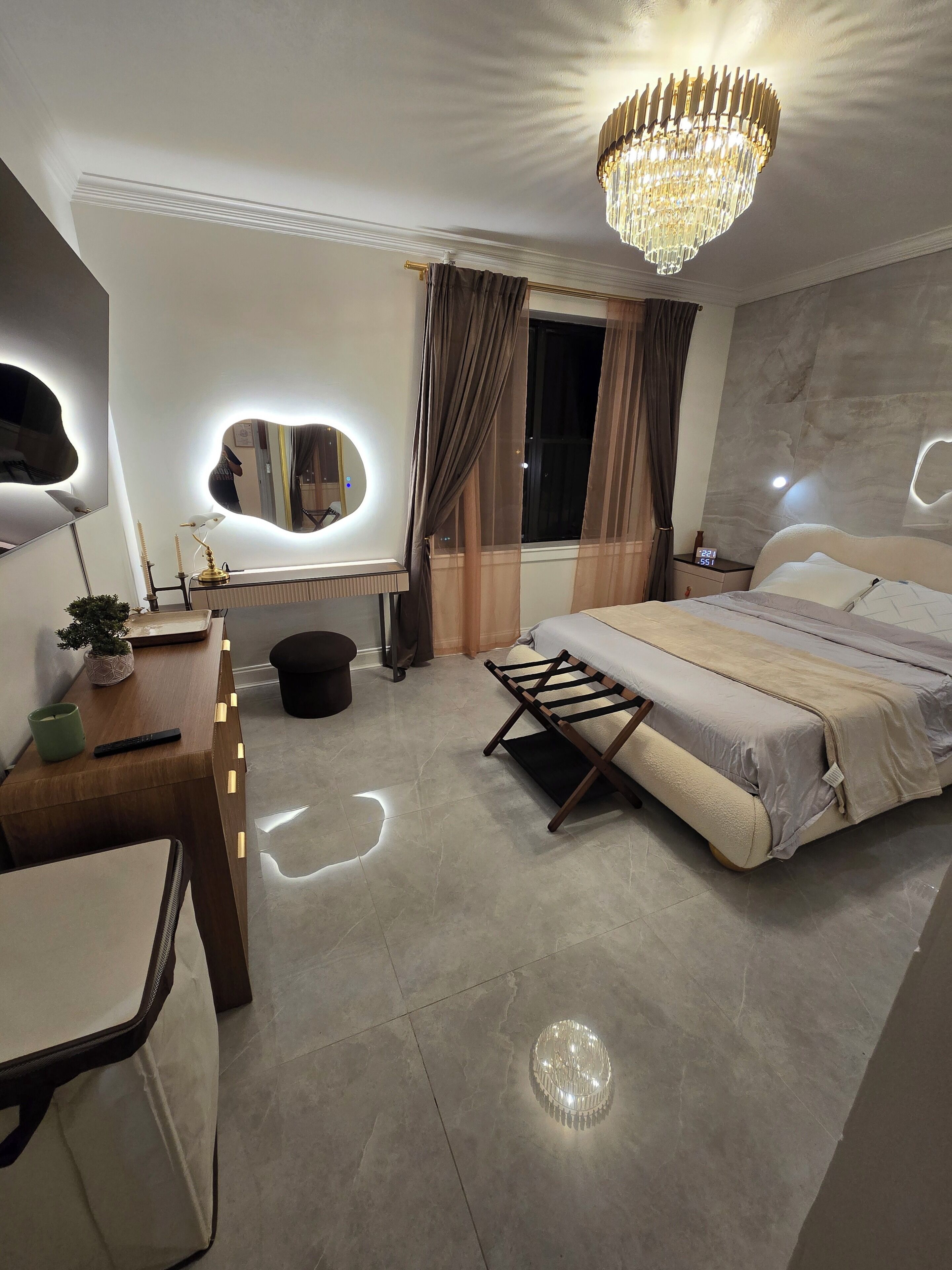 A modern bedroom with a large bed, bedside tables, a desk, and a chandelier.