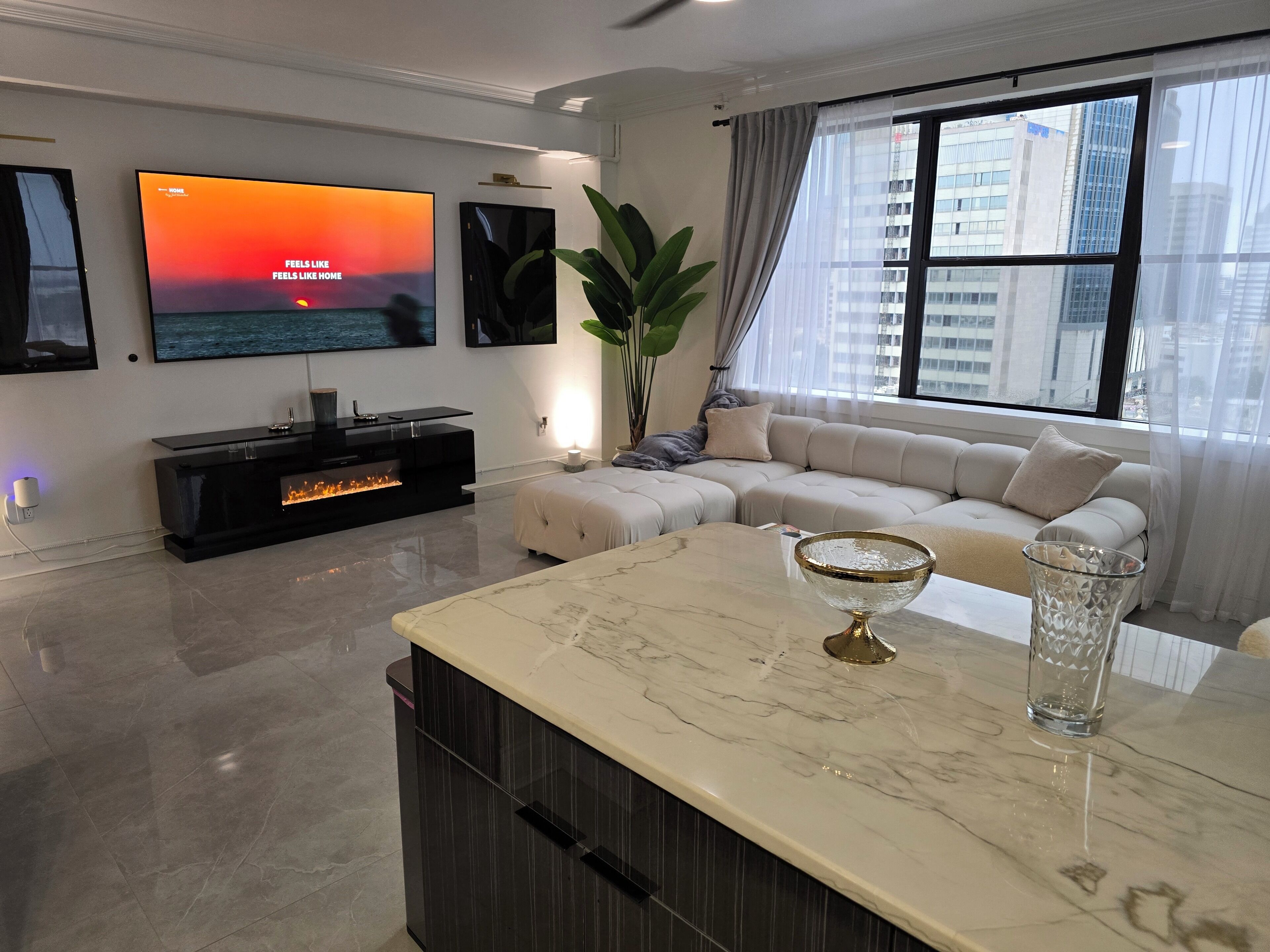 A modern living room with a flat-screen TV, a fireplace, a sectional sofa, and a marble coffee table.