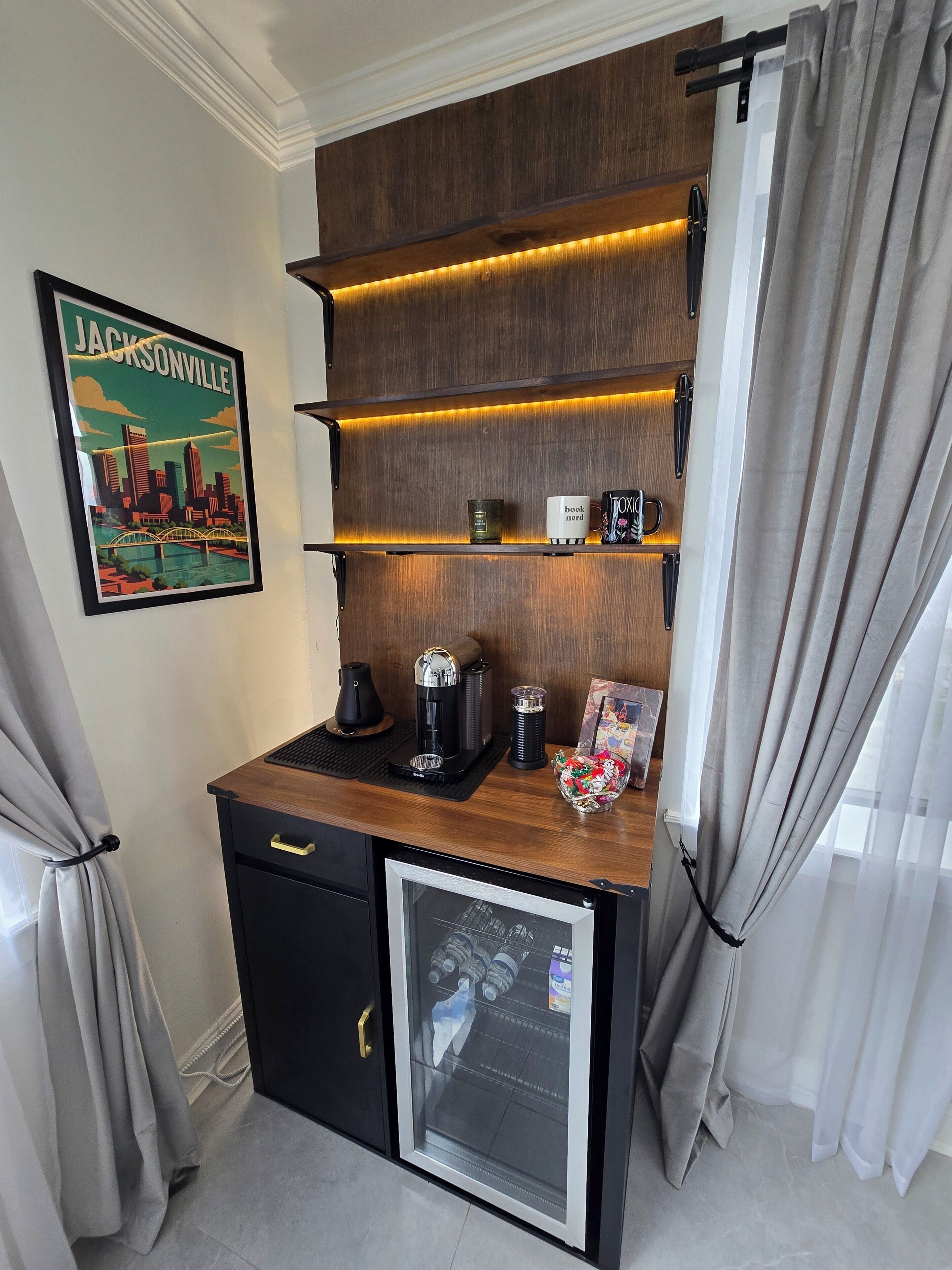 Una kitchenette compacta con cafetera, una taza y un refrigerador pequeño.