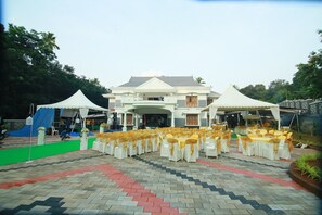 An outdoor event setup with a stage, chairs, and a tented area in front of a building.
