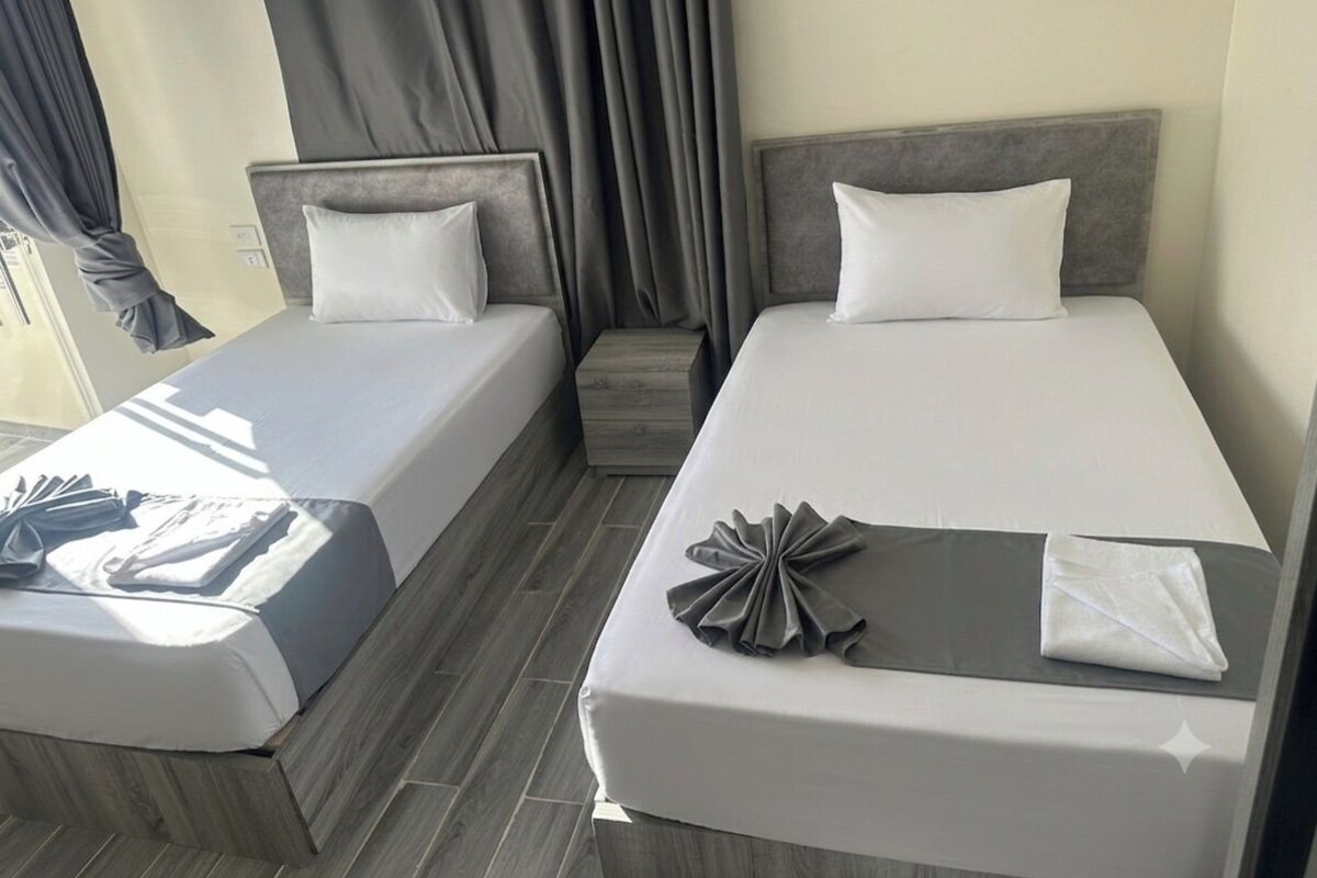 A hotel room with two beds, a small table, and a window with curtains.