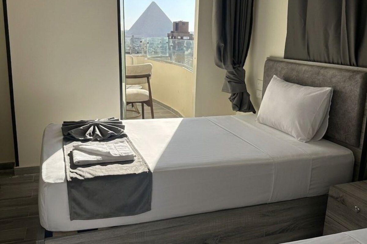 A hotel room with a bed, a view of a pyramid, and a balcony.