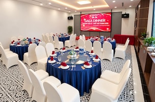 Un salón de conferencias con varias mesas redondas, sillas blancas y una pantalla grande que muestra un evento de cena de gala.