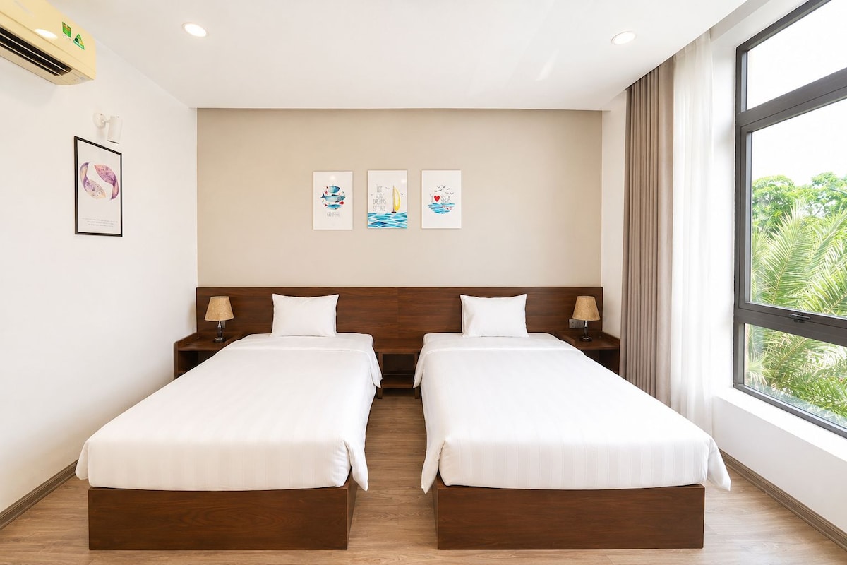A hotel room with two beds, a large window, and artwork on the wall.