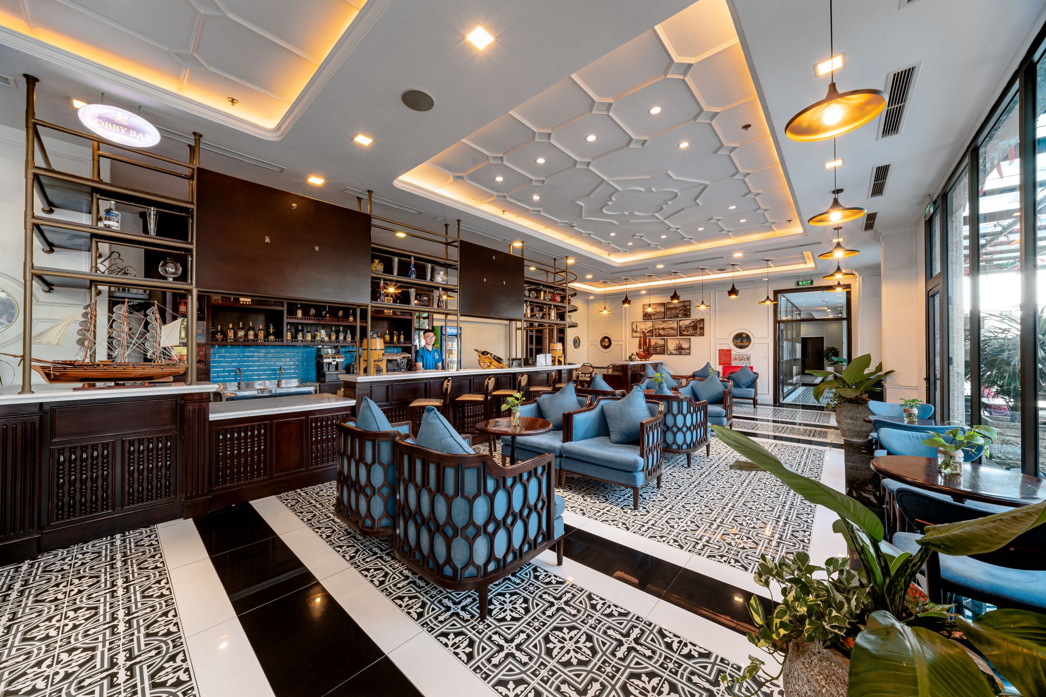 A modern bar area with seating and a bar counter, featuring geometric ceiling design and pendant lighting.