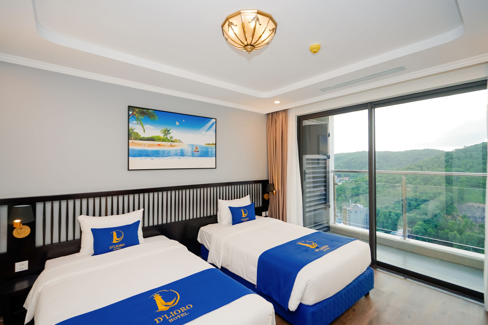 A hotel room with two beds, a painting of a beach scene, a large window with a city view, and a ceiling light fixture.