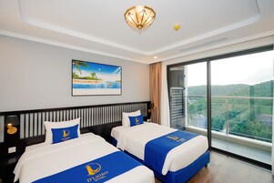 Habitación de hotel con dos camas, un cuadro de una playa, un ventanal con vista a la ciudad y una lámpara en el techo.