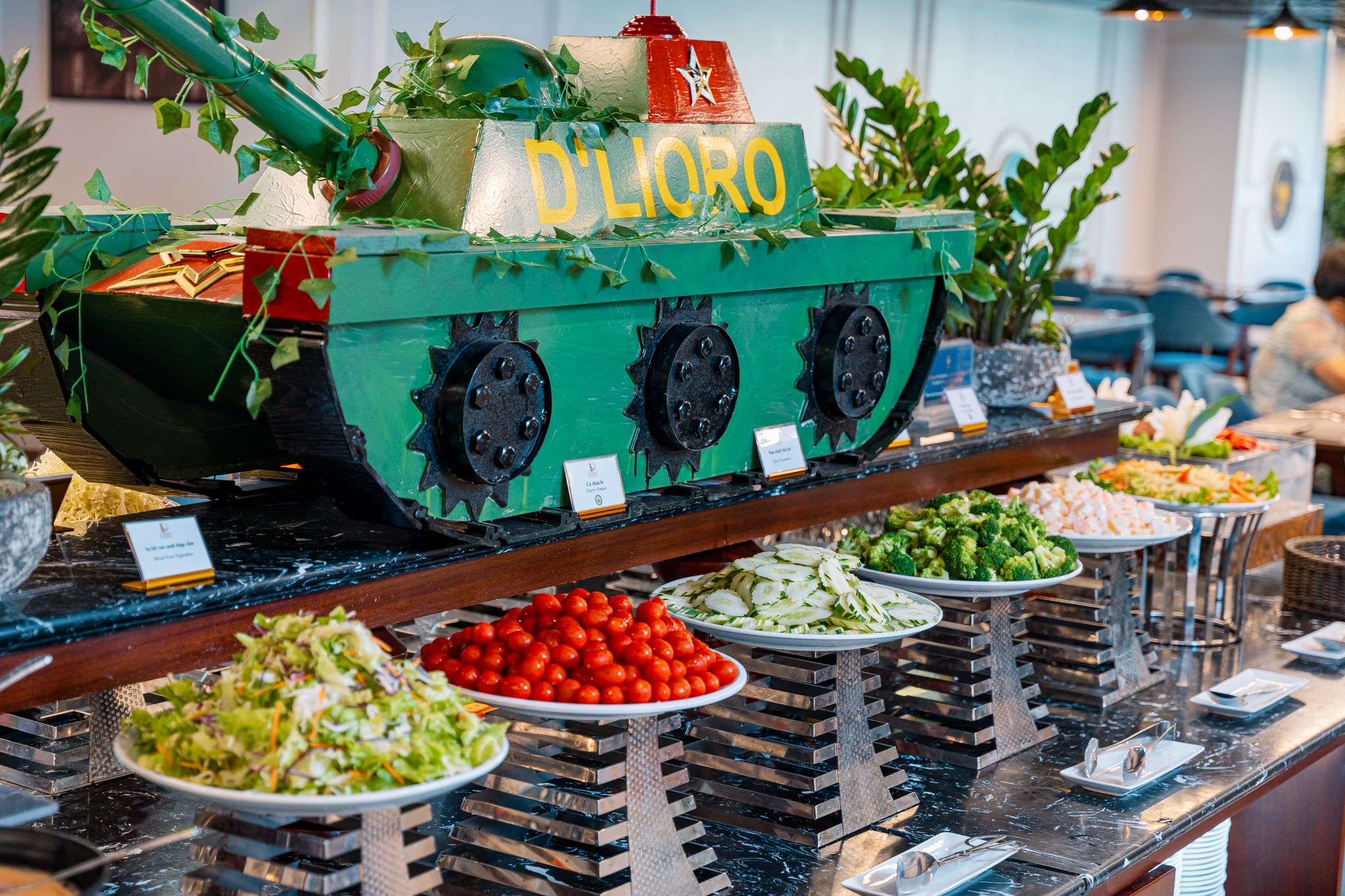 A buffet with various food items and a green tank-shaped decoration with the text 'D'LIORO'.