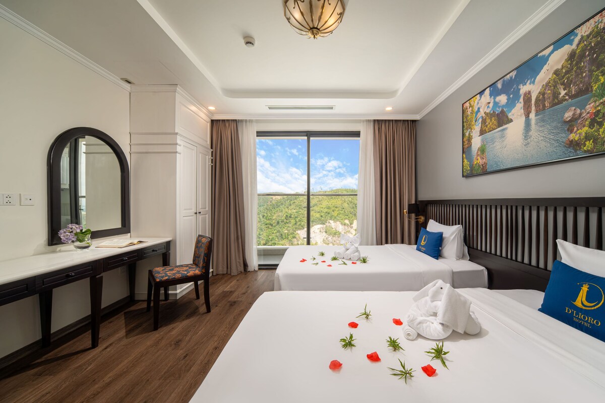 Habitación de hotel con escritorio, dos camas, un ventanal con vistas y un cuadro en la pared.