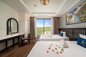 Habitación de hotel con escritorio, dos camas, un ventanal con vistas y un cuadro en la pared.