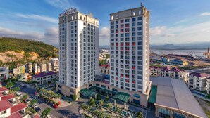 A high-rise hotel with multiple floors, a prominent sign at the top, and a view of the surrounding urban landscape. - D'lioro Hotel And Resort (Ha Long)