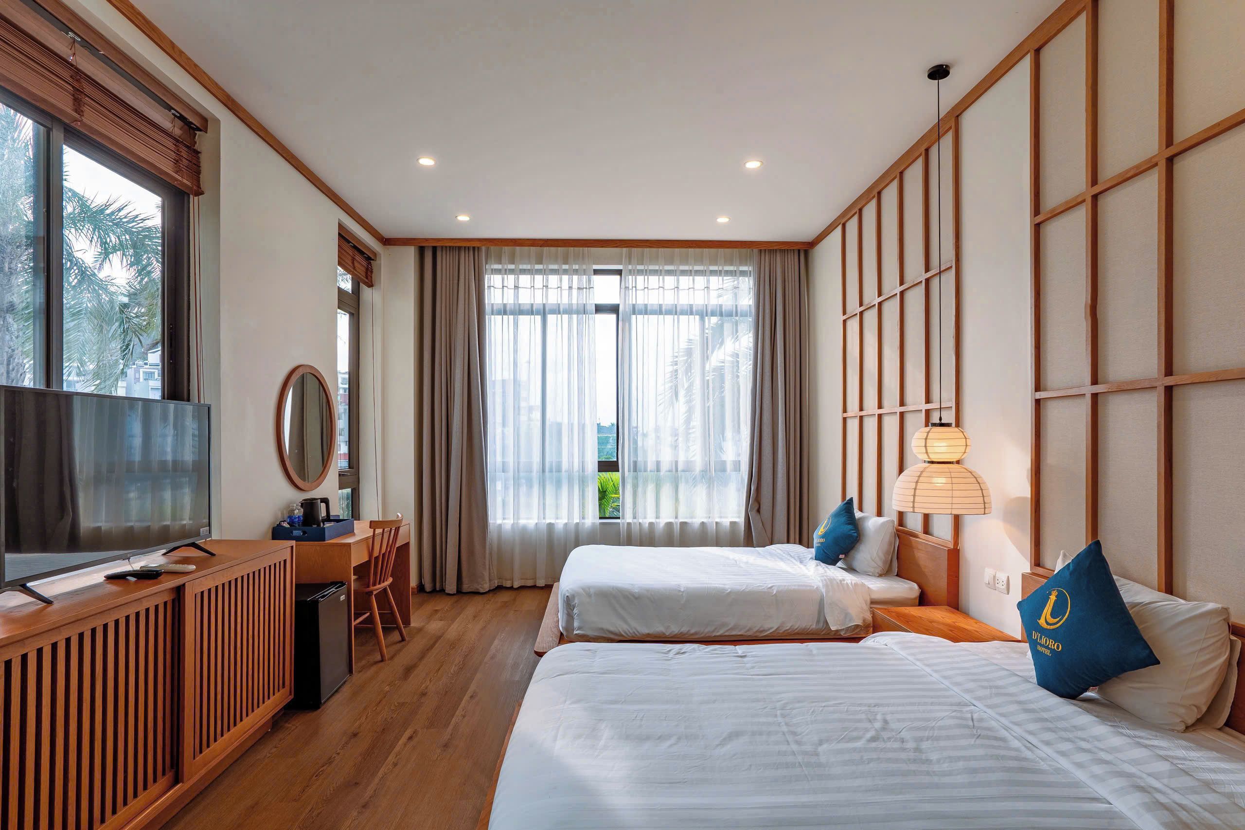 A hotel room with two beds, a desk, a chair, a TV, and a large window with curtains.