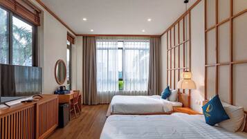 A hotel room with two beds, a desk, a chair, a TV, and a large window with curtains.