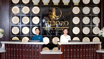 A hotel reception desk with multiple clocks displaying different city times, a reception area with two staff members, and a large emblem above the reception desk.